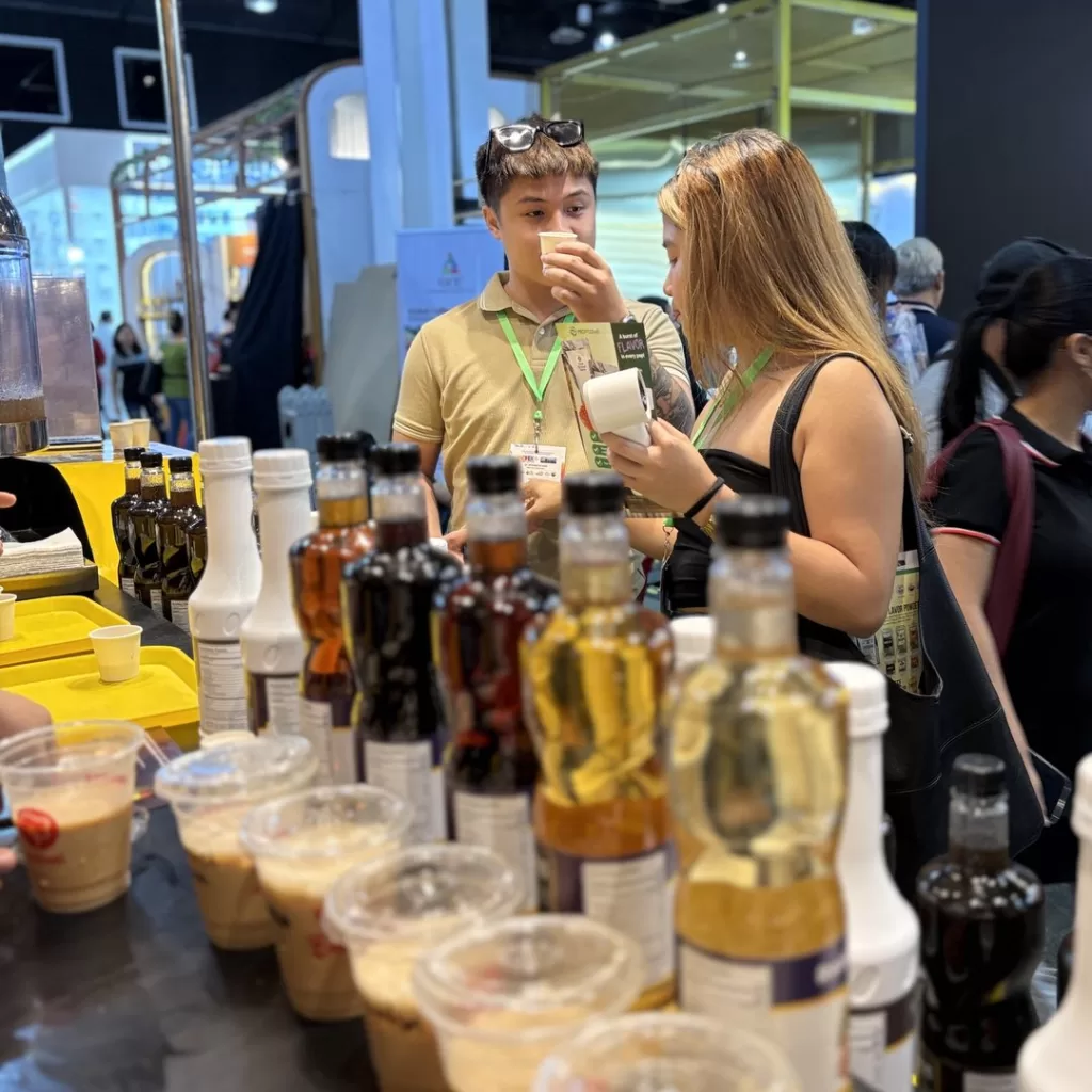 Event attendees sampling Divin’s drinks at WOFEX 2025, with various syrup bottles and prepared beverages displayed prominently, highlighting the use of real tea extract.