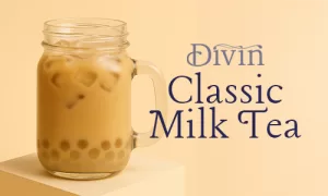 a mason jar filled with iced classic milk tea and lychee popping boba at the bottom, placed on a podium with a beige background