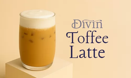 A glass of iced Toffee Latte topped with smooth cold foam, placed on a beige podium against a warm background.